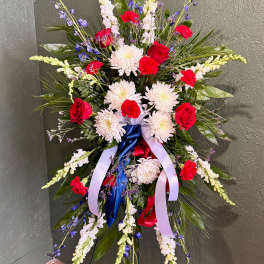 Tall standing spray of red roses, white mums, and blue accents with patriotic ribbons on an easel.