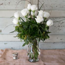 White roses in a clear glass vase with greenery