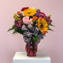 Mixed bouquet of sunflowers, roses, and purple flowers in a red vase