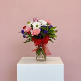 Bouquet of pink and white flowers in a glass vase with a red ribbon