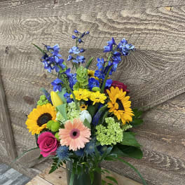 Mixed bouquet in a glass vase with sunflowers, roses, and blue flowers