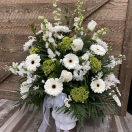 White and green floral arrangement in a white vase with a ribbon