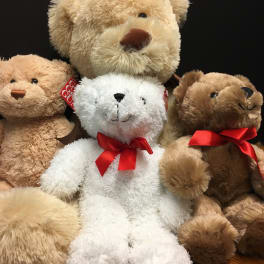 Assorted teddy bears with red bows on a wooden surface