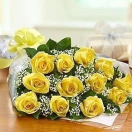 Wrapped bouquet of yellow roses with white filler flowers and a yellow ribbon bow
