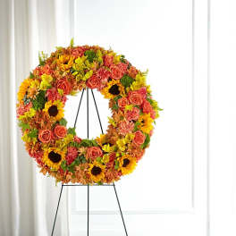Circular floral wreath on a black stand with sunflowers and roses
