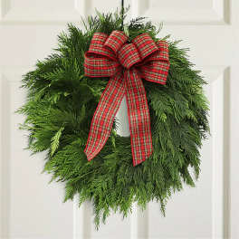 Green holiday wreath with a red plaid bow on a white door
