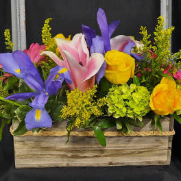 Colorful floral arrangement in a wooden box with yellow roses and purple irises