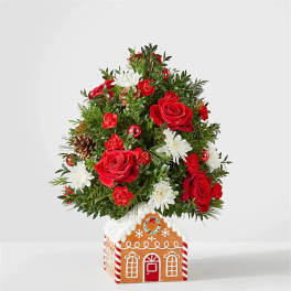 Christmas tree arrangement with red roses and white daisies in a gingerbread house container