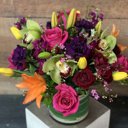 Bright mixed bouquet with roses, tulips, orchids, and lilies in a green vase