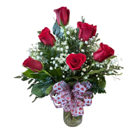Arrangement of red roses and white filler flowers in a glass vase with a heart-pattern bow