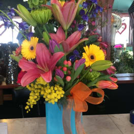 Tall mixed flower arrangement in a blue vase with orange ribbon