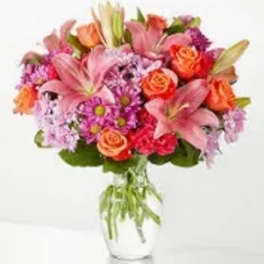 Mixed bouquet of pink lilies, orange roses, and purple flowers in a glass vase