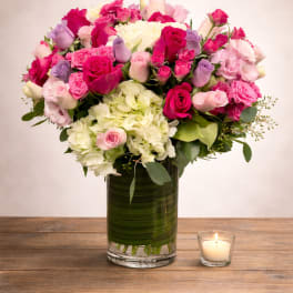Pink and white rose bouquet in a glass vase beside a lit candle