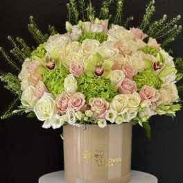 Round bouquet of pale roses and green orchids in a beige hatbox