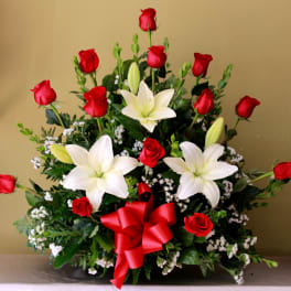 Red roses and white lilies in a low arrangement with a red ribbon bow