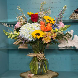 Mixed bouquet in a glass vase with roses, hydrangea, sunflowers, and orchids