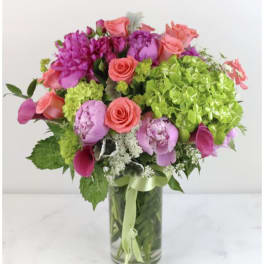 Bouquet of pink and coral flowers in a clear glass vase with a green ribbon