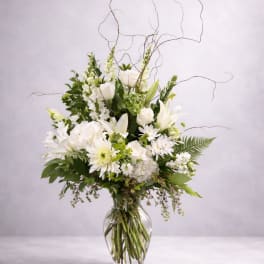 White floral arrangement in a clear glass vase with curly branches