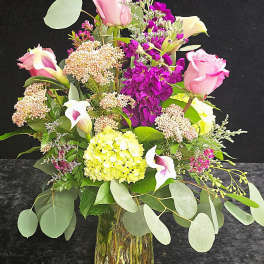 Mixed bouquet of pink roses, purple blooms, white calla lilies and pale hydrangea in a glass vase