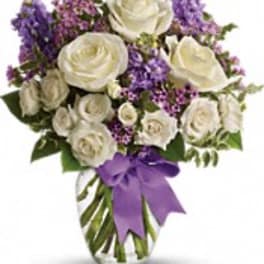 White roses and purple flowers in a clear glass vase with a purple ribbon