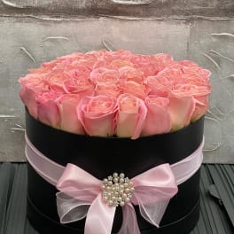 Round black hatbox filled with pink roses and tied with a pink ribbon bow
