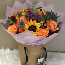 Bouquet of orange roses, sunflowers, and purple blooms in pink wrap