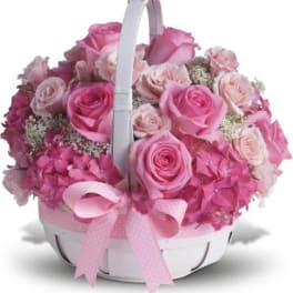 Pink roses and hydrangeas in a white basket with a pink ribbon