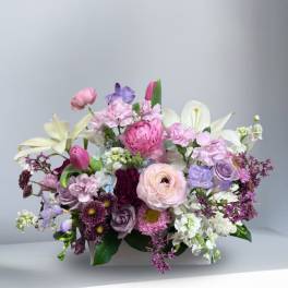 Mixed pink, purple, and white floral arrangement in a low white container