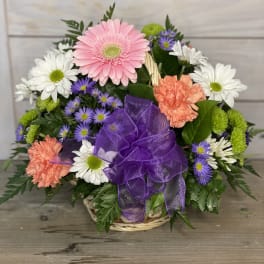 Mixed bouquet of daisies, gerbera, and carnations in a basket with a purple bow