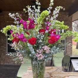 Tall bouquet of red roses and pink flowers in a clear glass vase