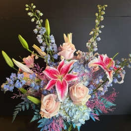 Bouquet of pink lilies, pale roses, and blue flowers in a glass vase