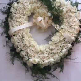 White floral wreath with a ribbon bow and dark greenery