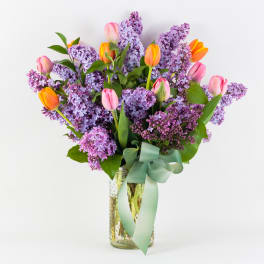 Bouquet of purple lilacs and pink tulips in a glass vase with a ribbon