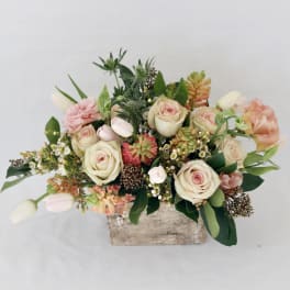 Mixed bouquet of pale roses, tulips, and peach blooms in a rustic wooden container