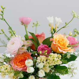 Mixed bouquet of roses, ranunculus, and white blooms in a rustic container