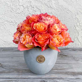 Orange and pink roses arranged in a gray vase