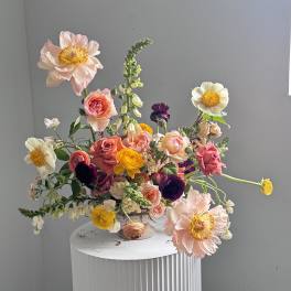 Mixed bouquet of pink, yellow, white, and purple flowers in a pedestal vase