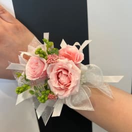 Pink rose wrist corsage with white ribbon and green accents