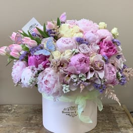 Pink and white floral arrangement in a round box with butterfly picks