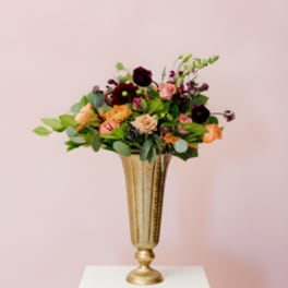 Mixed flower arrangement in a gold vase on a white pedestal