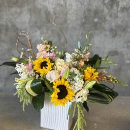 Mixed floral arrangement with sunflowers and roses in a white vase
