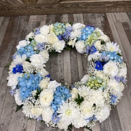 Circular floral wreath of white and blue flowers on a wood floor