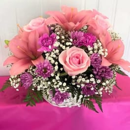Pink lilies and roses in a white basket with purple filler flowers