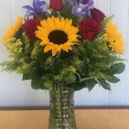 Bouquet of sunflowers, red roses, and purple irises in a glass vase