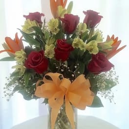 Bouquet of red roses and orange lilies in a glass vase with a bow