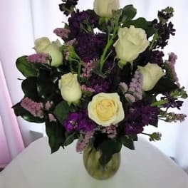 Bouquet of cream roses and purple flowers in a glass vase