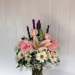 Pink roses and lilies arranged in a glass vase with white daisies