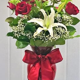Red roses and a white lily in a vase with a red ribbon
