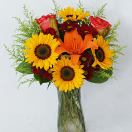 Bouquet of sunflowers, orange lilies, and red roses in a glass vase