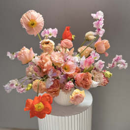 Loose bouquet of peach, pink, and coral flowers in a white vase